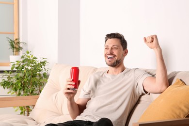 Photo of Happy handsome man with can of beverage on sofa indoors