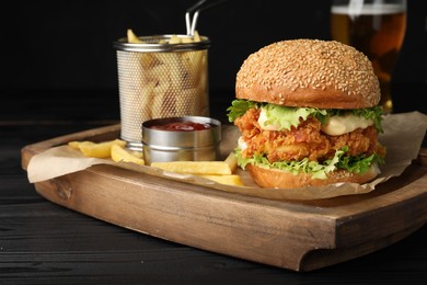 Photo of Delicious burger with crispy chicken patty, french fries and sauce on black wooden table