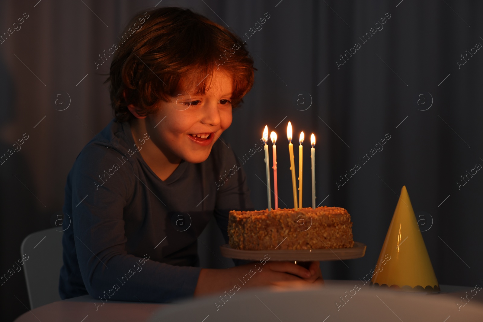 Photo of Cute boy with birthday cake at table indoors