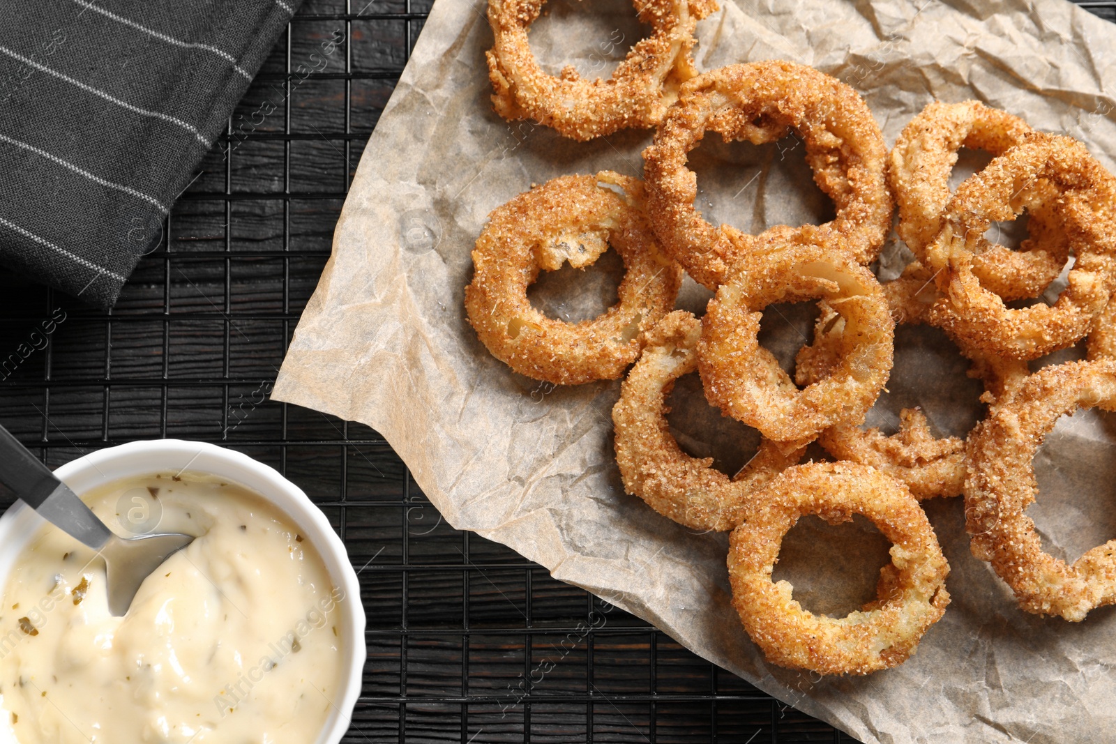 Photo of Cooling rack with homemade crunchy fried onion rings and sauce on wooden background, top view