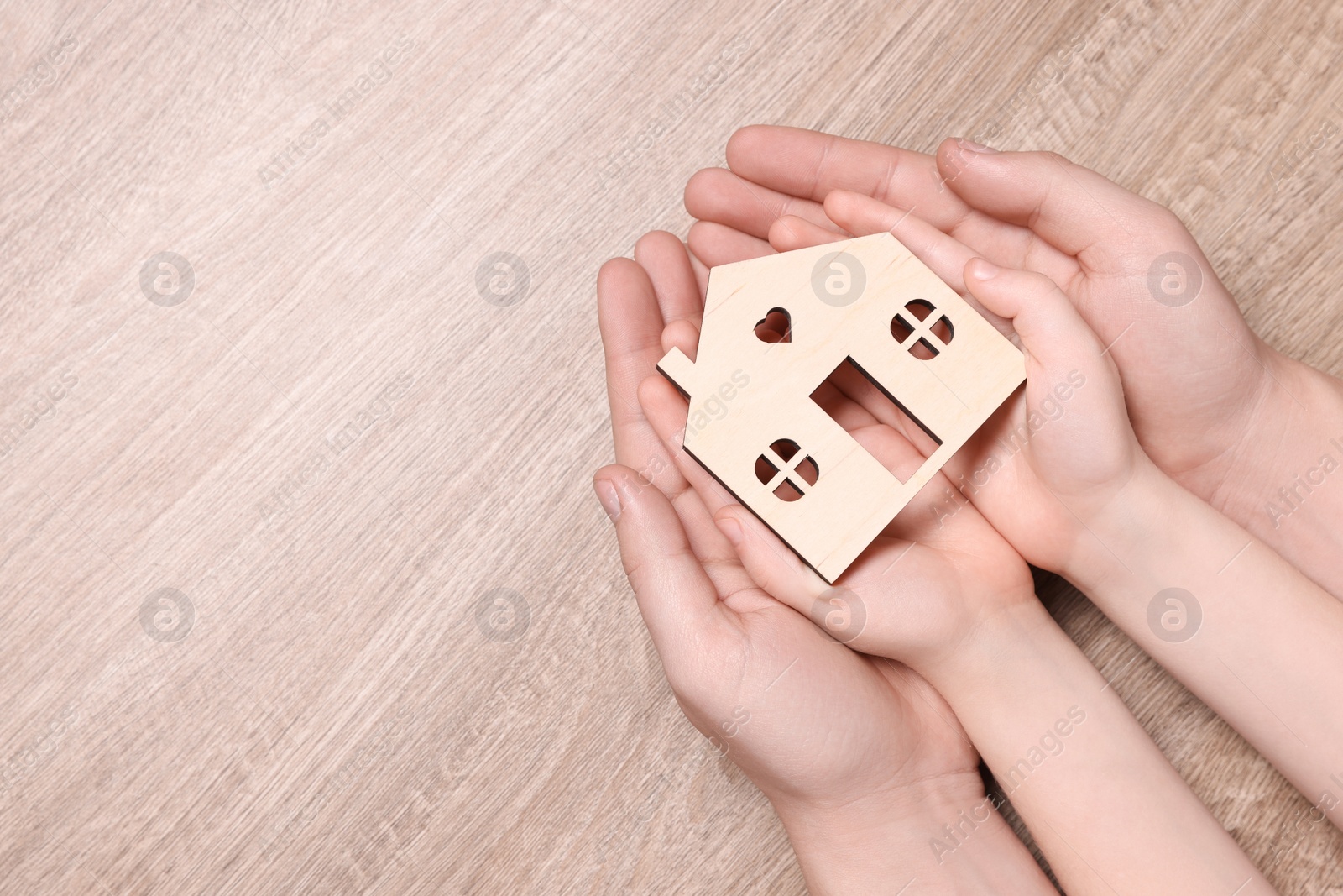 Photo of Home security concept. Man and his little child holding house model at wooden table, top view with space for text