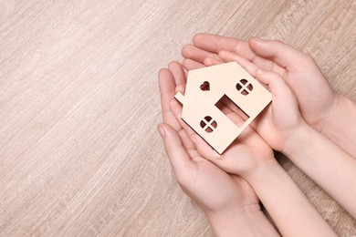 Home security concept. Man and his little child holding house model at wooden table, top view with space for text