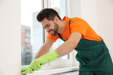 Photo of Professional young janitor cleaning windowsill in room