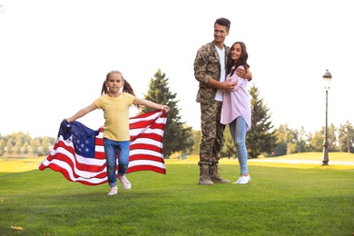 Photo of Little girl running with American flag, her father in military uniform and mother at sunny park