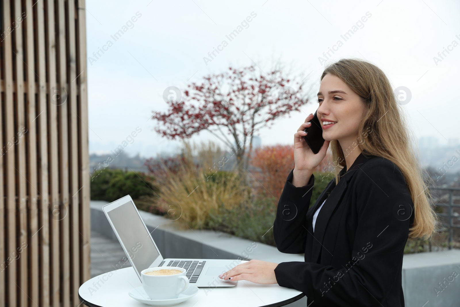 Photo of Businesswoman with laptop talking on phone in outdoor cafe. Corporate blog