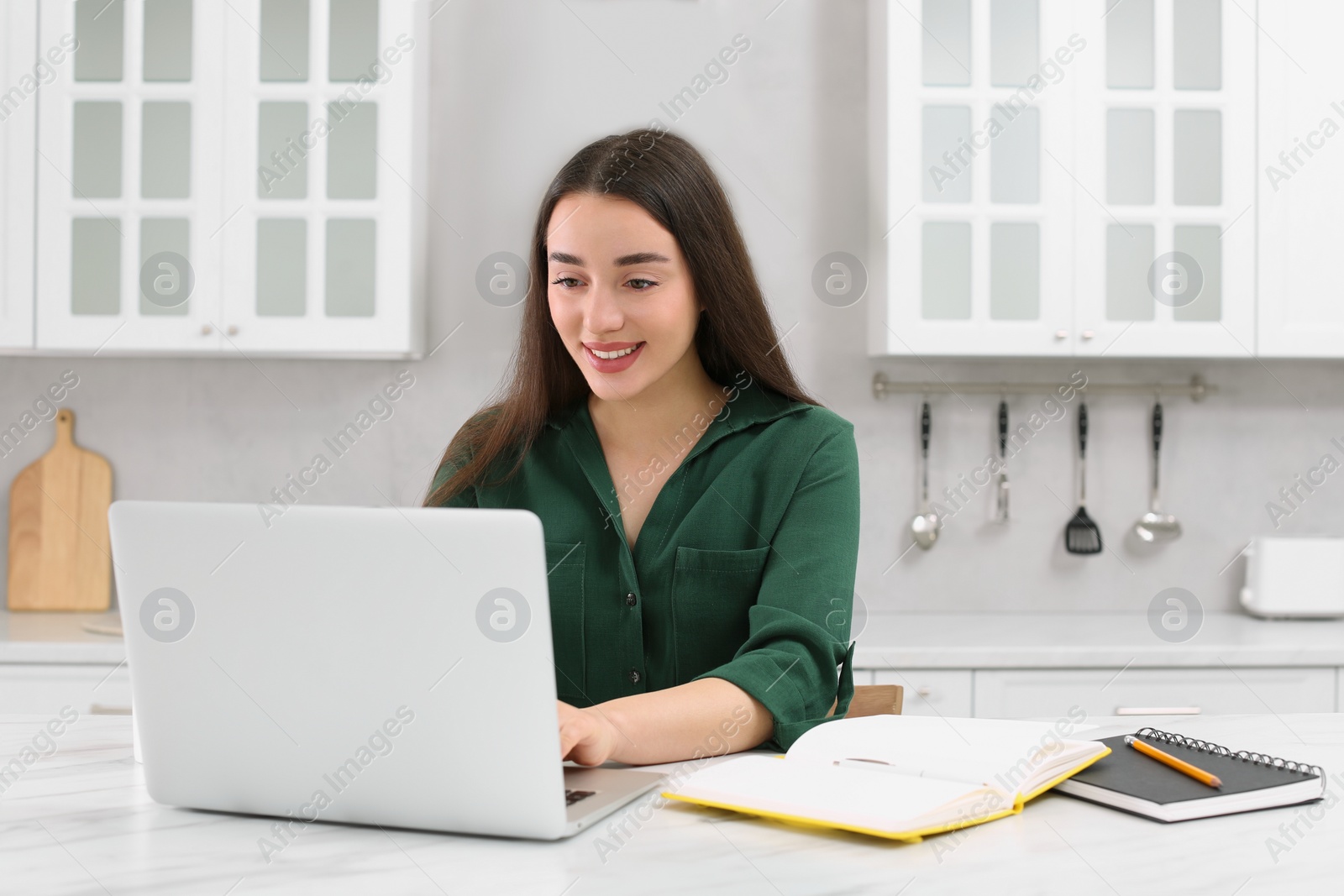 Photo of Home workplace. Happy woman typing on laptop at marble desk in kitchen