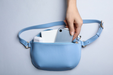 Photo of Woman taking smartphone from small bag on light grey background, top view