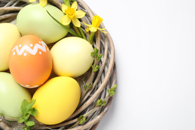 Photo of Colorful Easter eggs in decorative nest on white background, top view