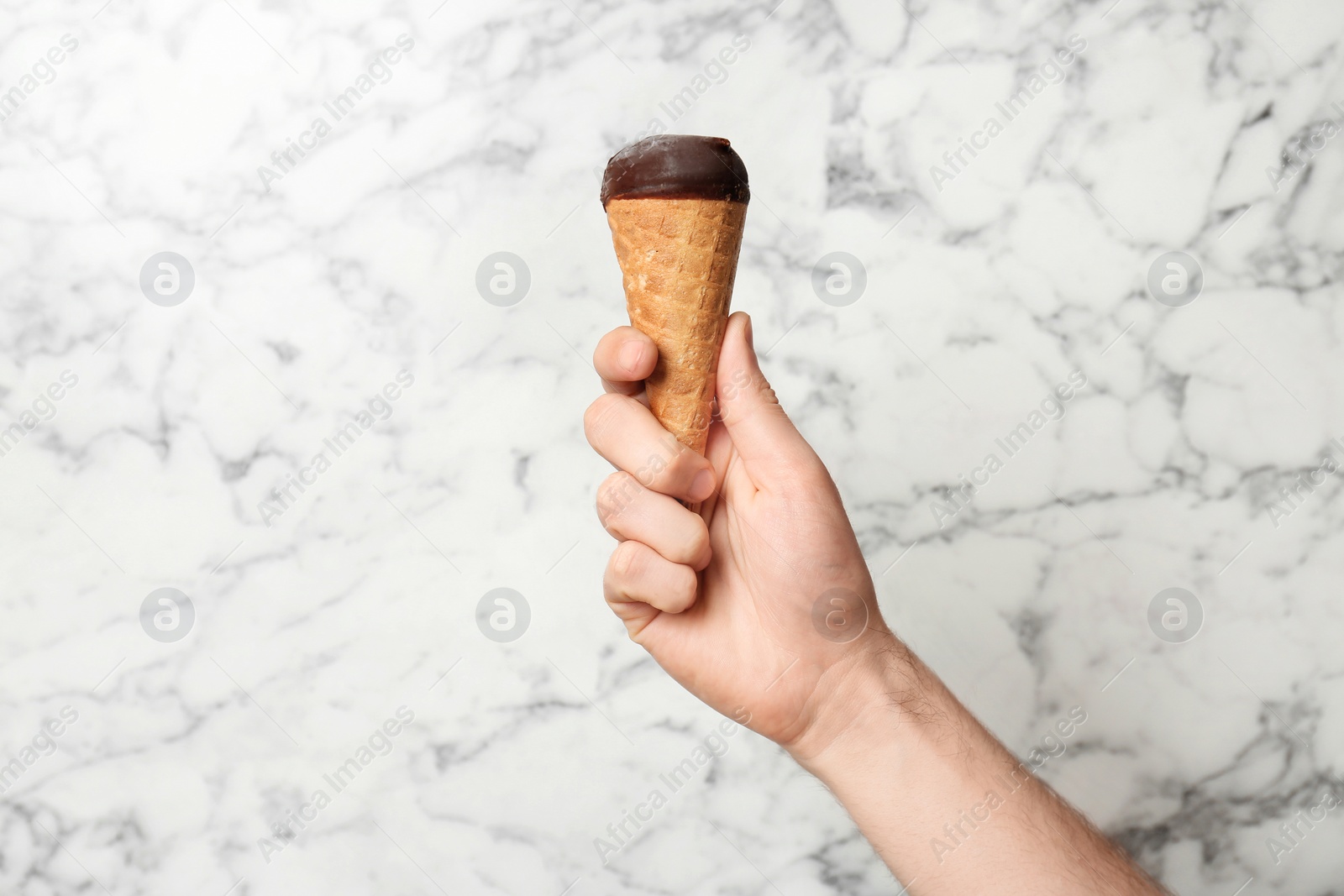 Photo of Man holding yummy ice cream on marble background. Focus on hand