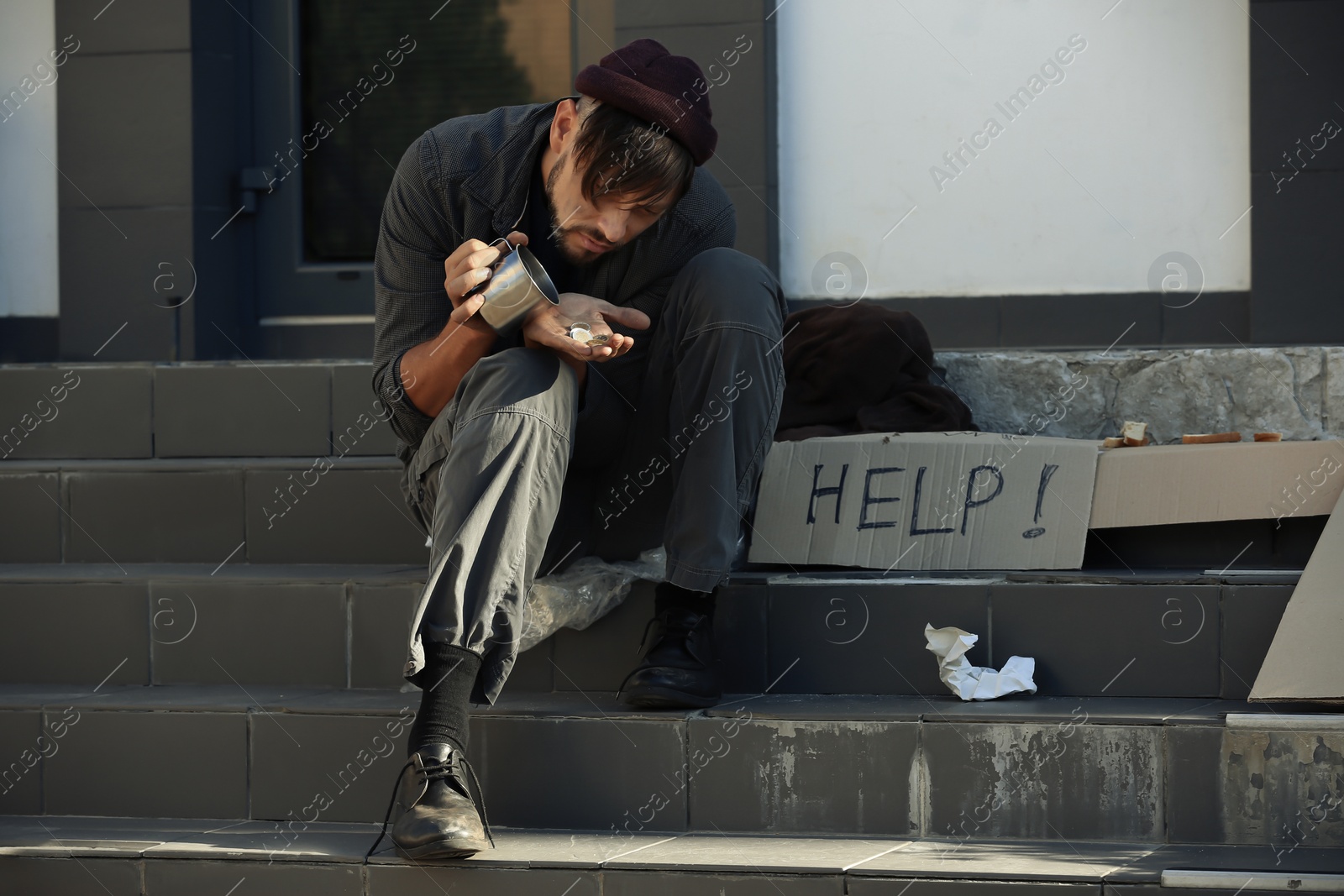 Photo of Poor man with mug counting coins on city street