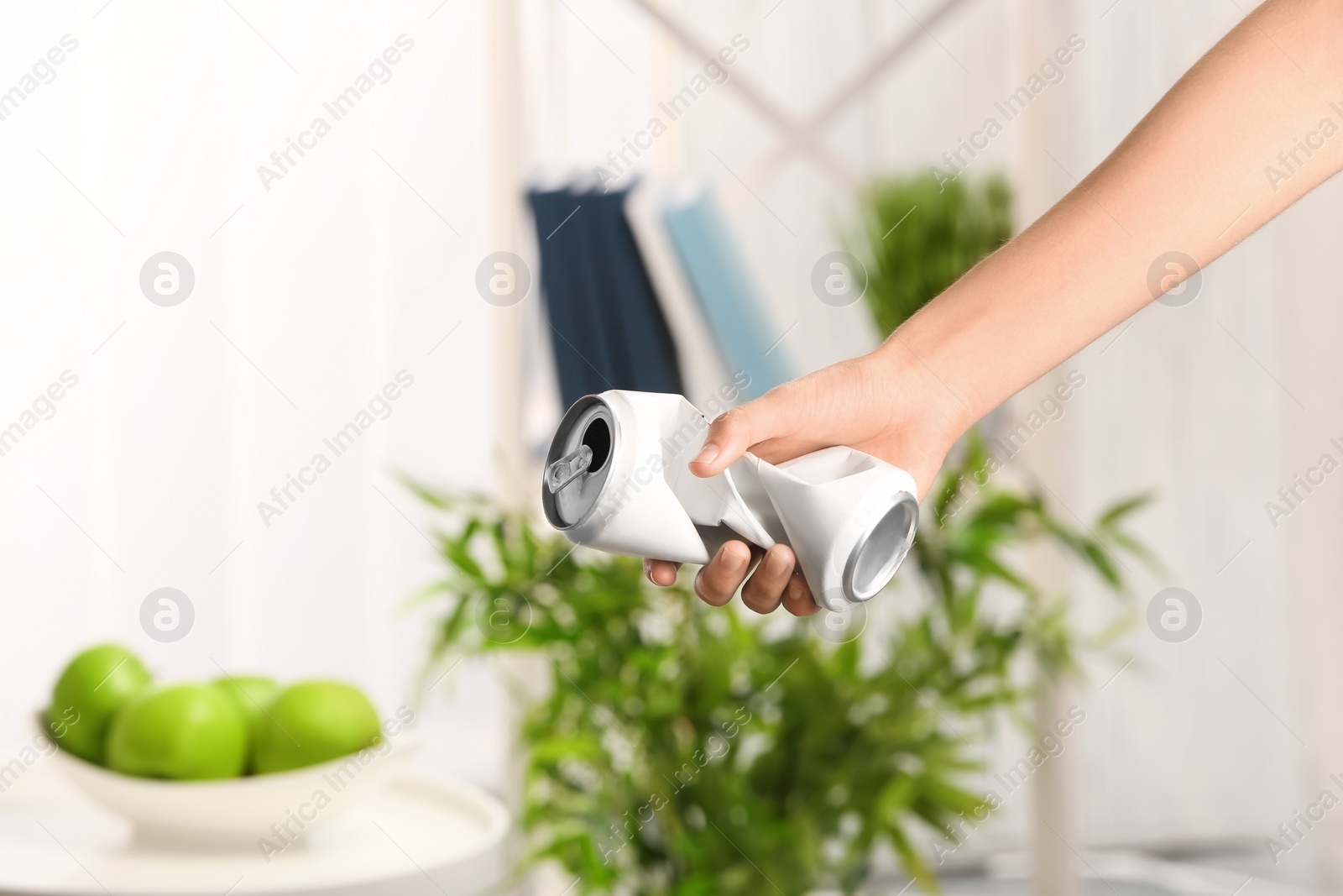 Photo of Woman holding crumpled aluminum can on blurred background. Metal waste recycling