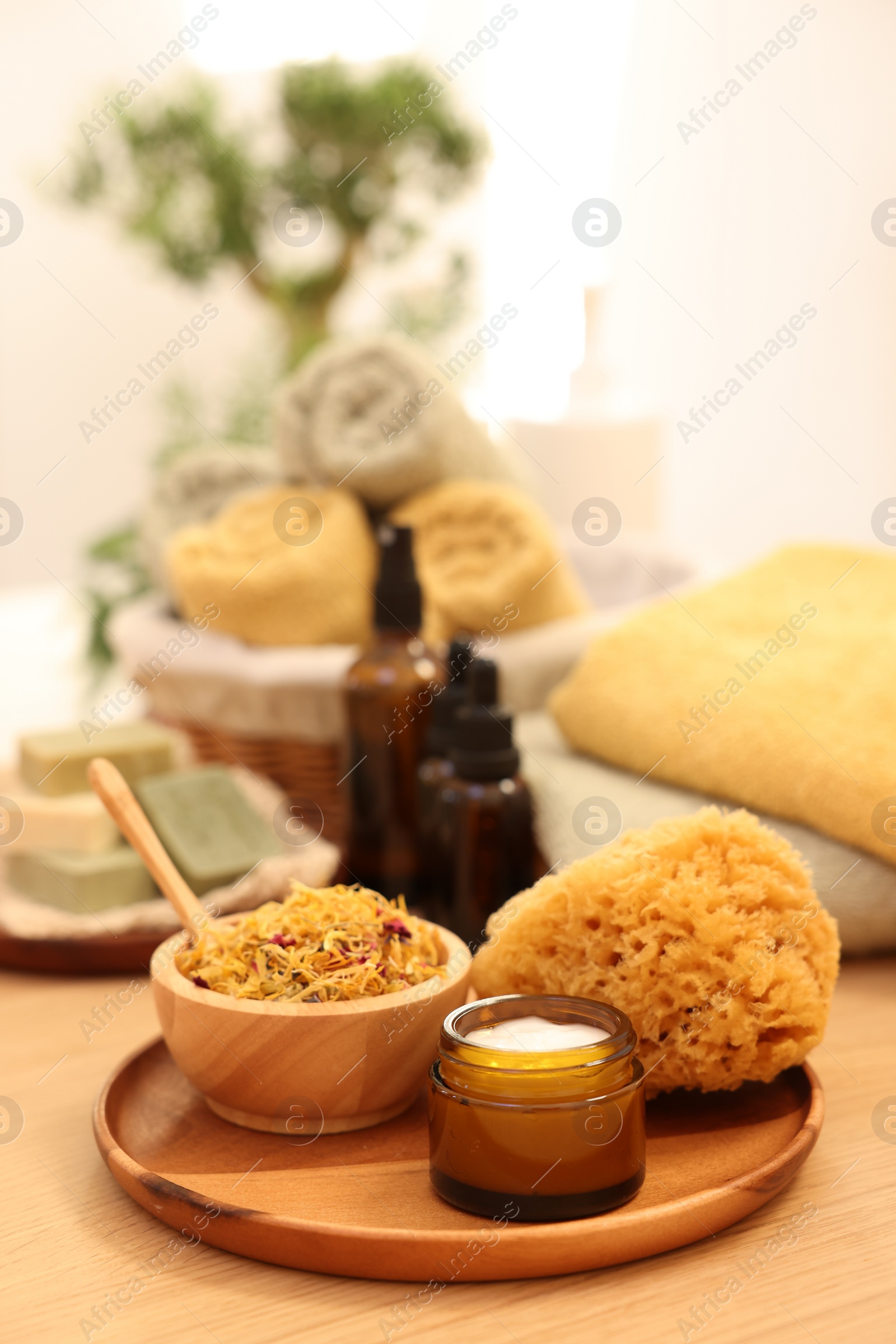 Photo of Loofah, dry flowers and jar with cream on wooden table indoors. Spa time