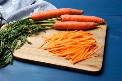Photo of Fresh ripe juicy carrot sticks and whole vegetables on blue wooden table