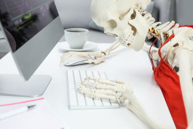 Human skeleton in red dress using computer at table, closeup