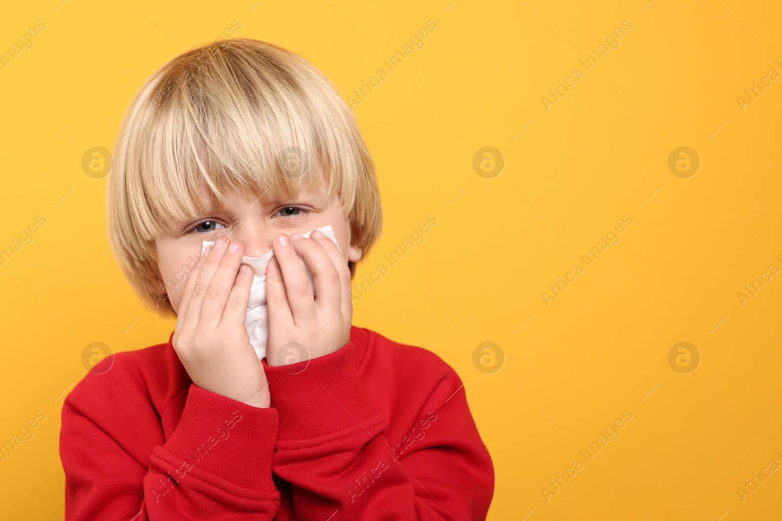 Photo of Boy blowing nose in tissue on orange background, space for text. Cold symptoms