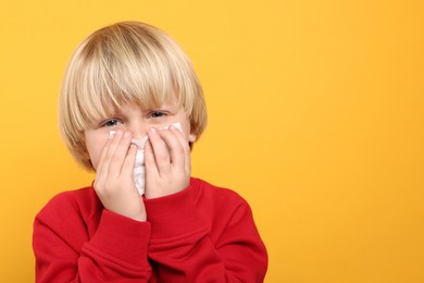 Photo of Boy blowing nose in tissue on orange background, space for text. Cold symptoms