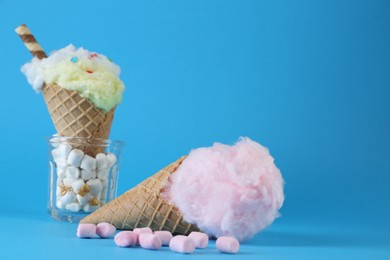 Sweet cotton candy in waffle cone and marshmallows on light blue background, closeup