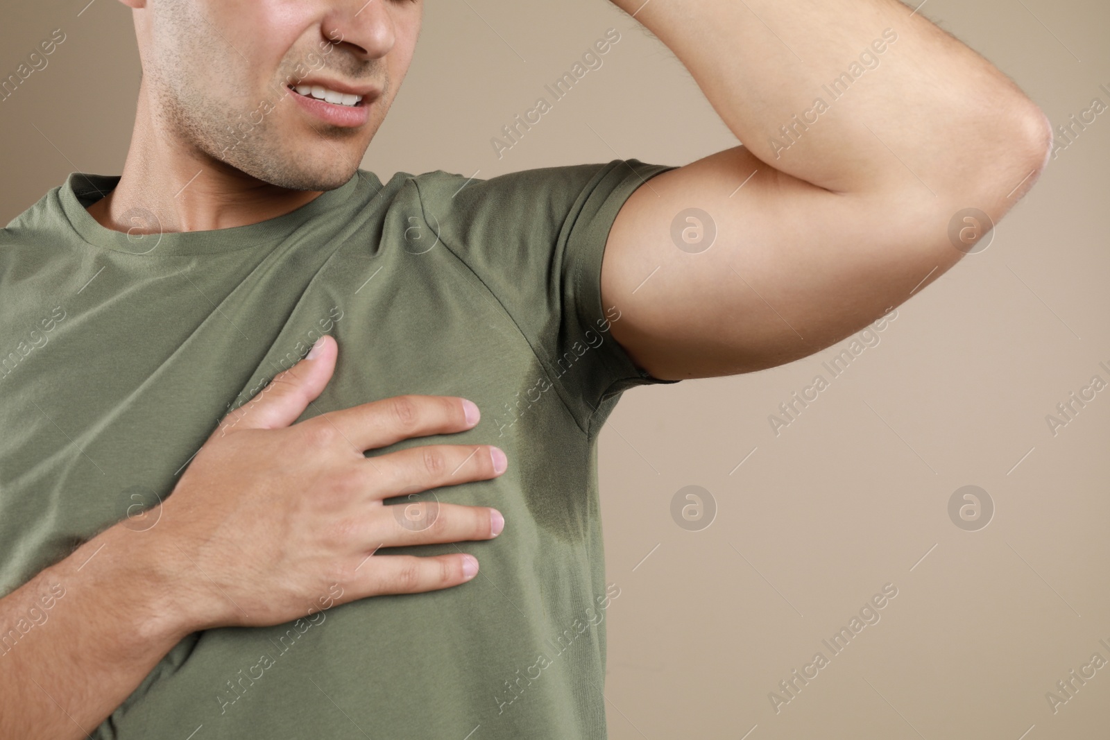 Photo of Young man with sweat stain on beige background, closeup. Using deodorant