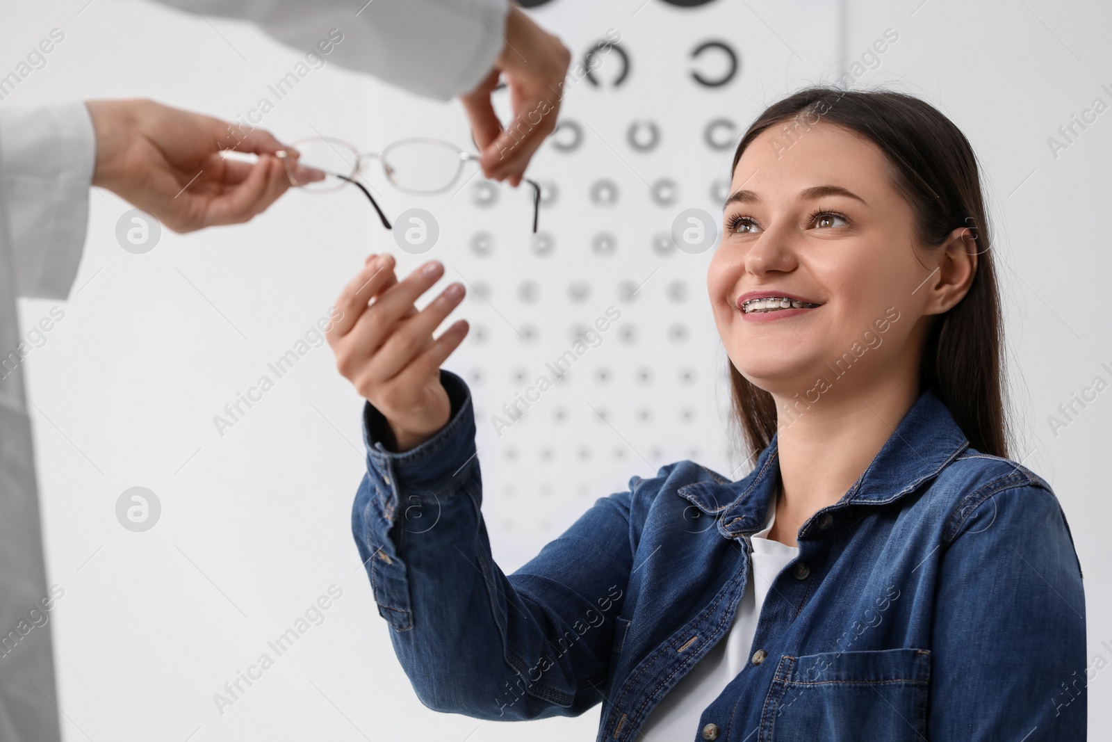 Photo of Vision testing. Ophthalmologist giving glasses to young woman indoors