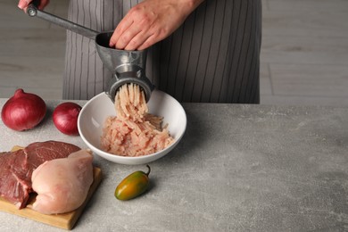 Woman making chicken mince with metal meat grinder at grey table indoors, closeup. Space for text