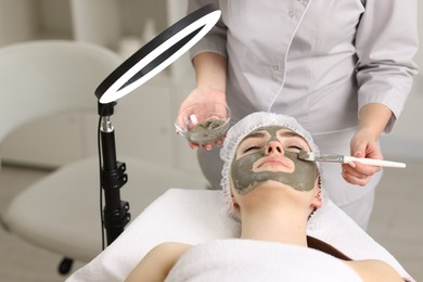 Photo of Cosmetologist applying mask on woman's face in clinic, closeup