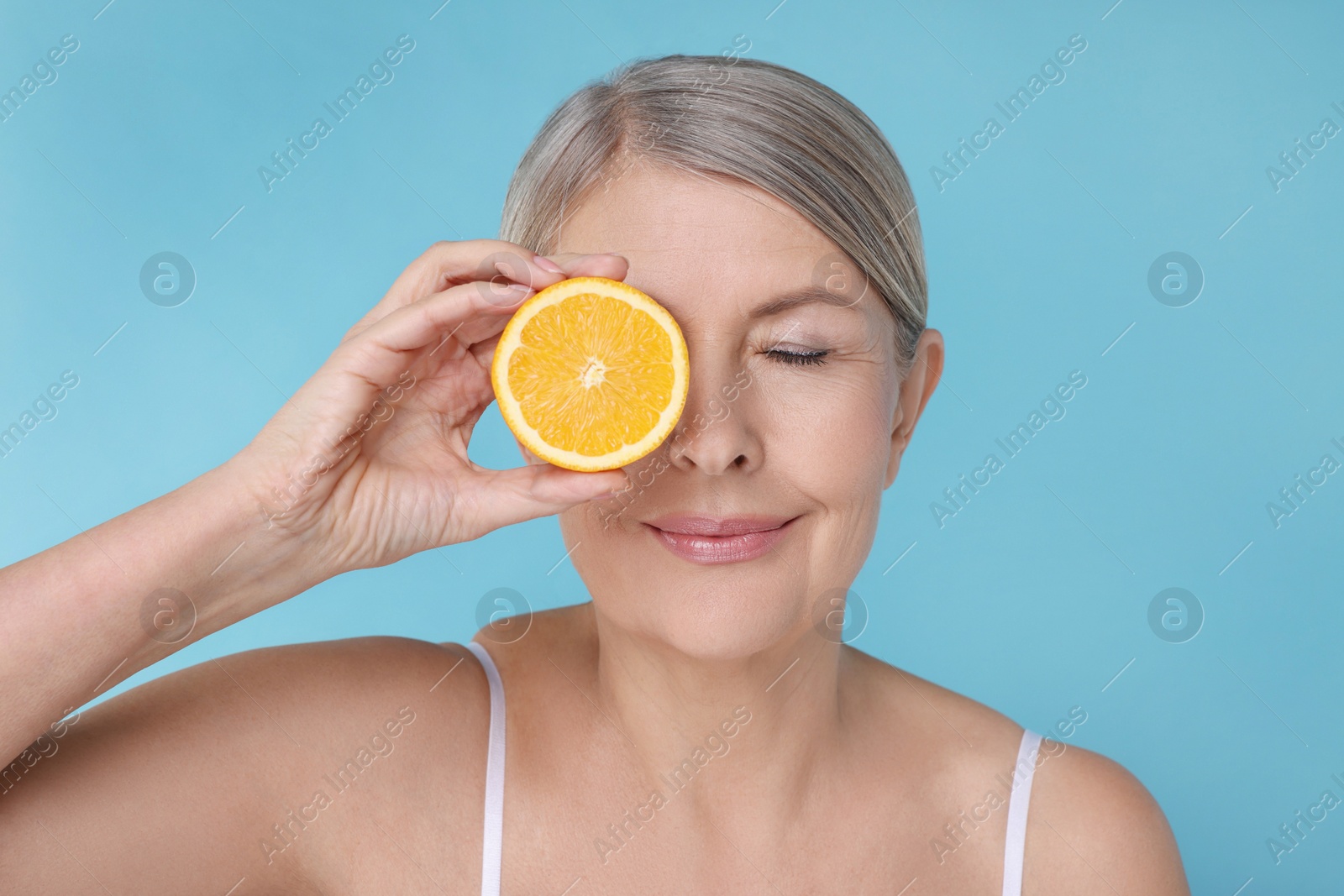 Photo of Beautiful woman with half of orange rich in vitamin C on light blue background