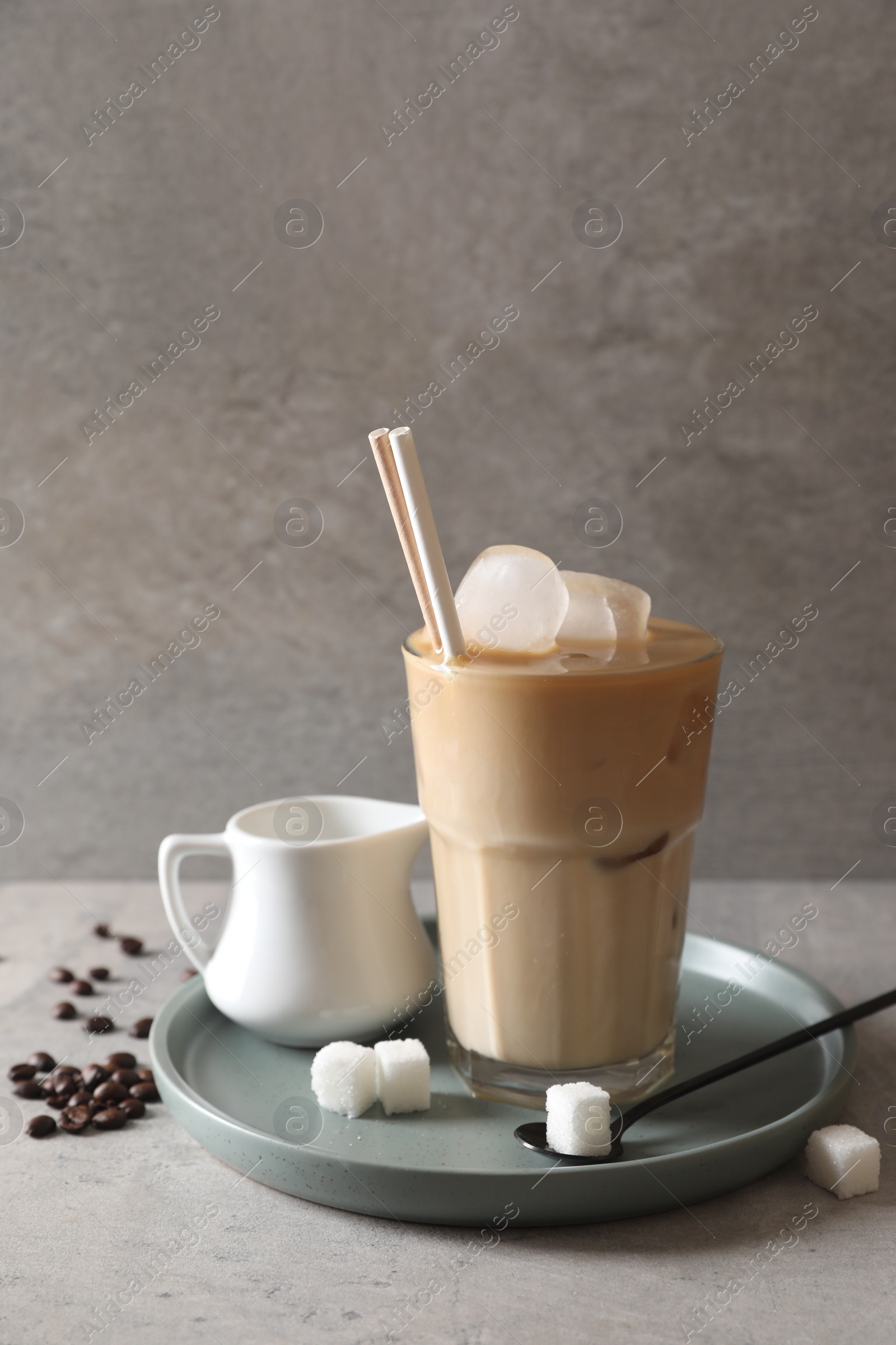 Photo of Refreshing iced coffee with milk in glass, sugar and spoon on gray table