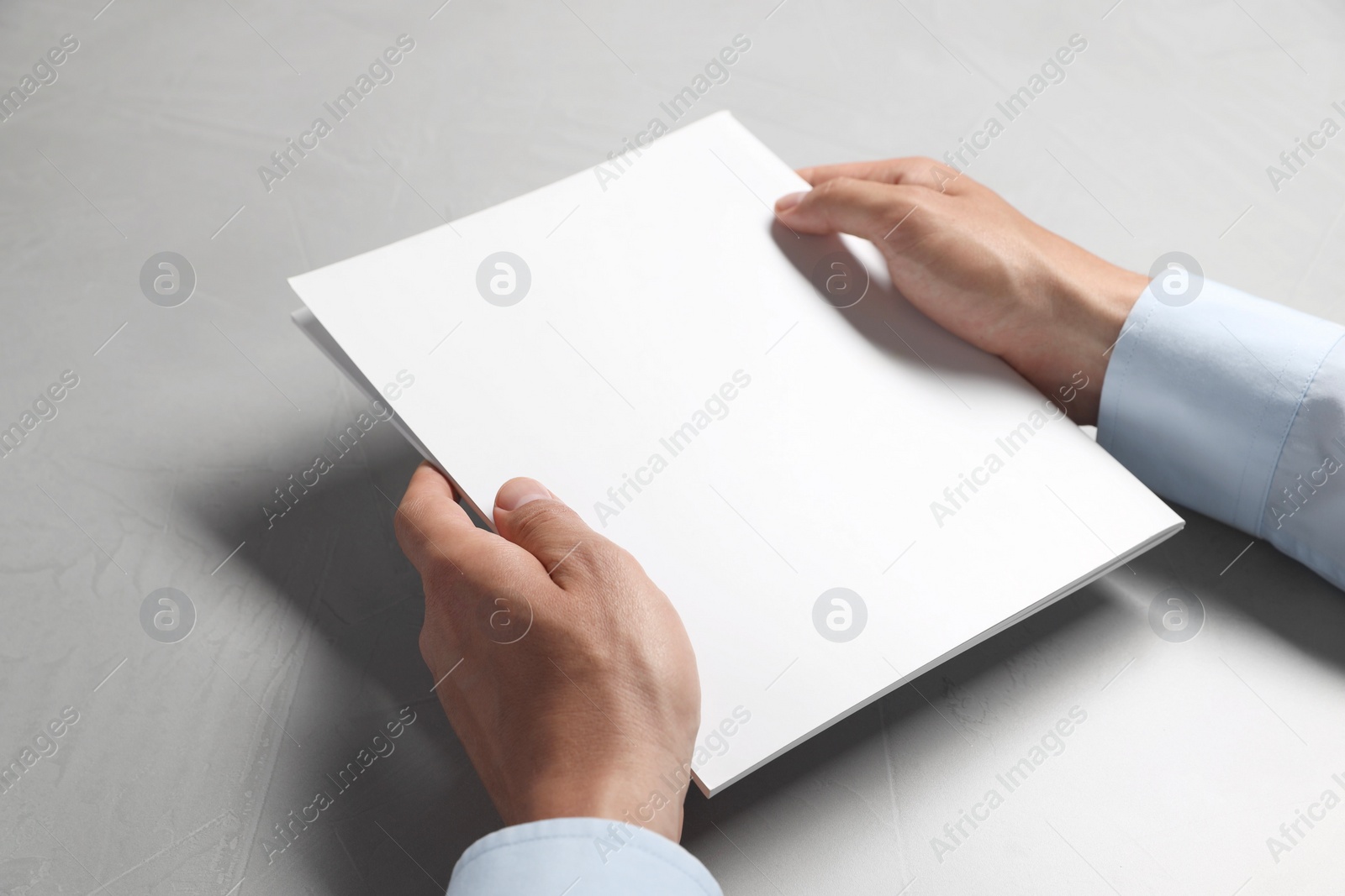 Photo of Man holding blank notebook at light grey table, closeup. Mockup for design