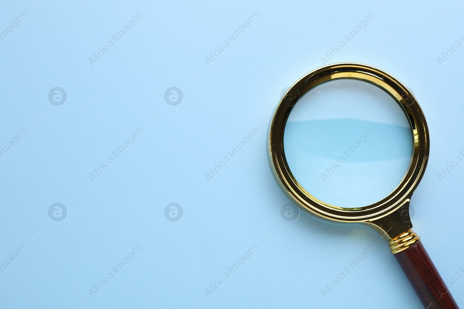 Photo of Magnifying glass on light blue background, top view. Space for text