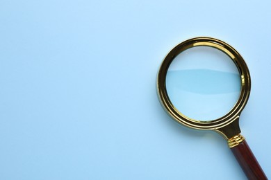 Magnifying glass on light blue background, top view. Space for text