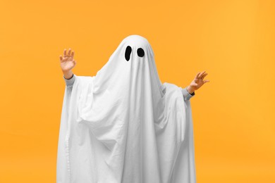 Photo of Child in white ghost costume on orange background. Halloween celebration