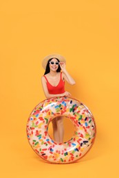 Happy young woman with beautiful suntan, hat, sunglasses and inflatable ring against orange background