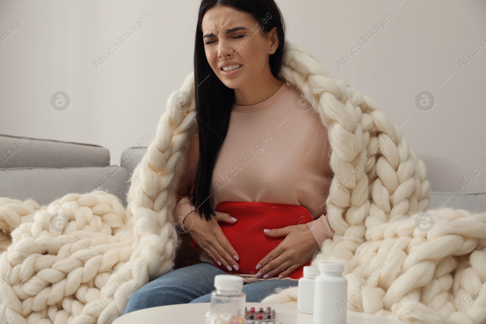 Photo of Woman using hot water bottle to relieve menstrual  pain on sofa at home