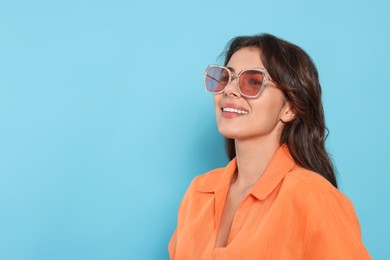 Happy beautiful woman with stylish sunglasses on light blue background, space for text