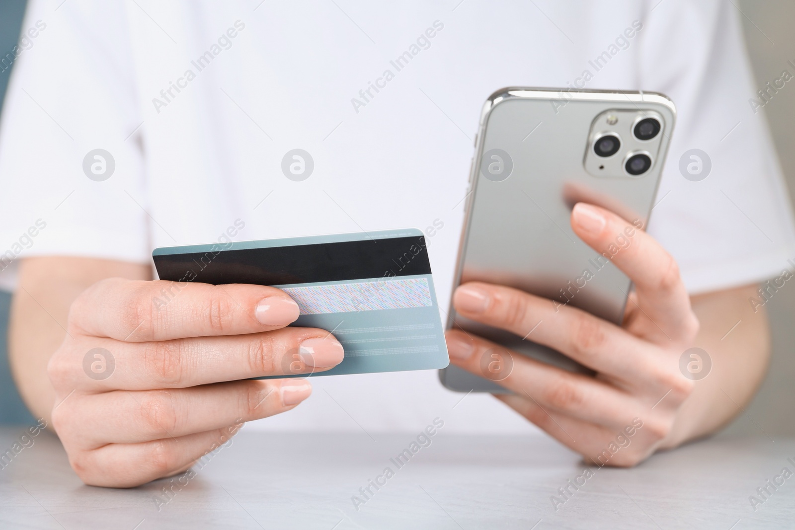 Photo of Online payment. Woman with smartphone and credit card at white table, closeup