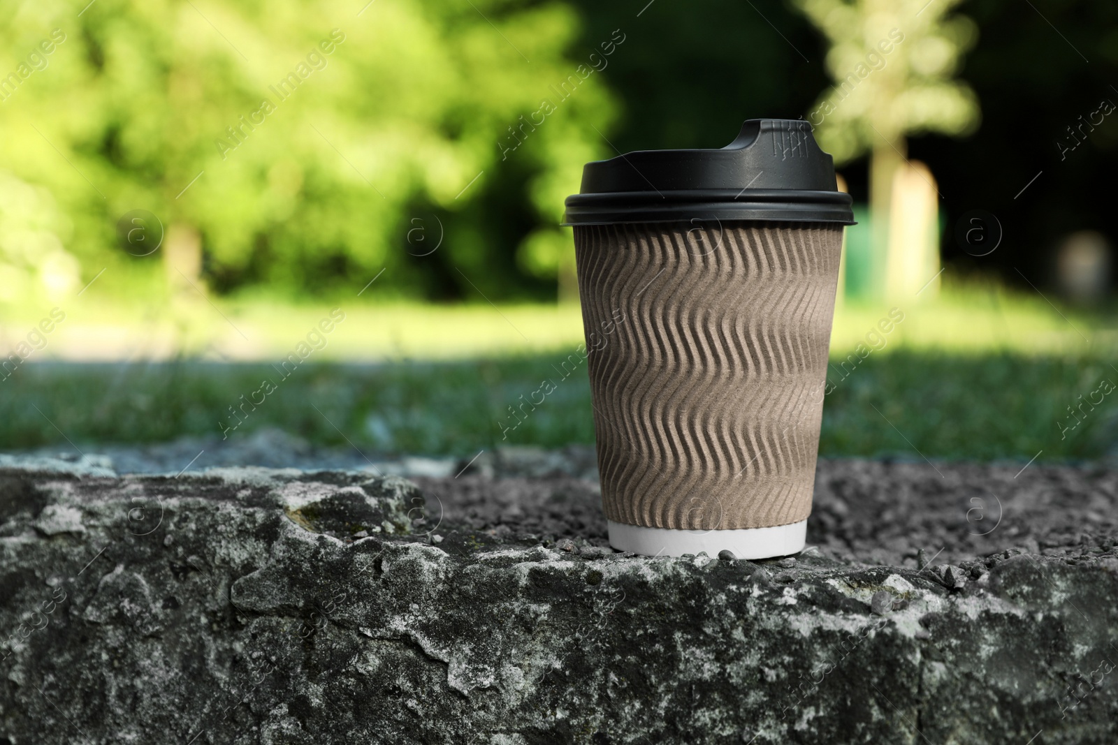 Photo of Cardboard takeaway coffee cup with plastic lid on stone surface outdoors, space for text