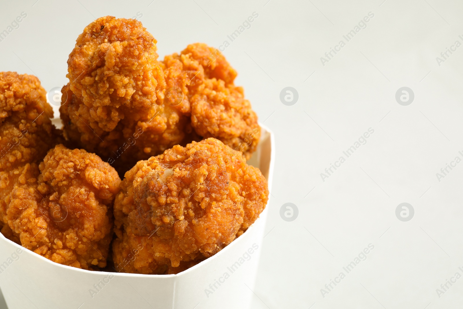Photo of Tasty deep fried chicken pieces on light background, closeup. Space for text