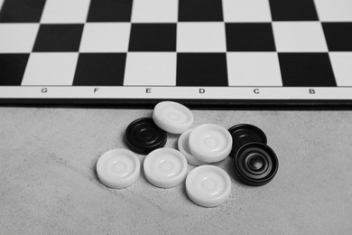 Photo of Checkerboard and game pieces on light grey table, closeup