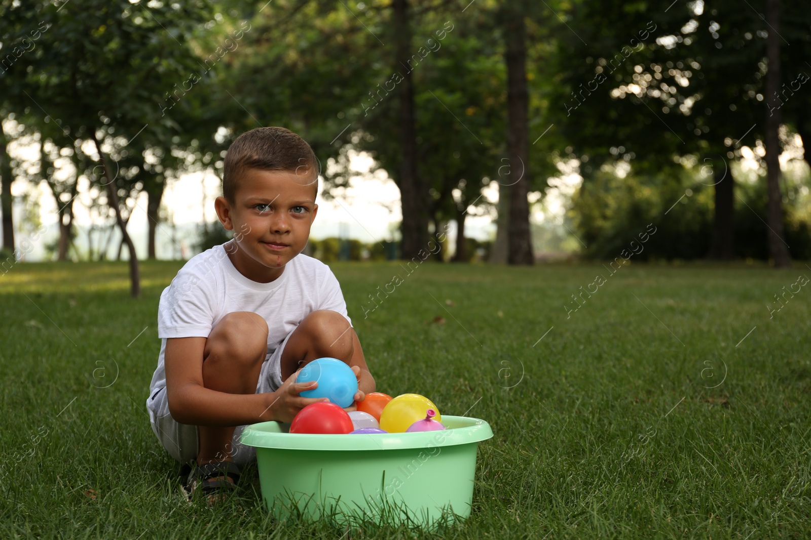 Photo of Little boy with basin of water bombs in park