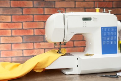 Photo of Sewing machine with fabric and craft accessories on wooden table against brick wall