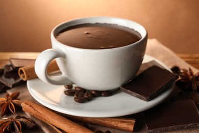 Photo of Cup of delicious hot chocolate, spices and coffee beans on wooden table