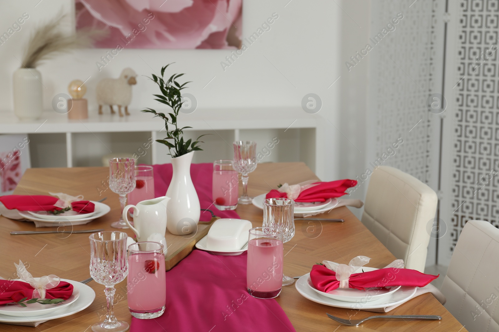 Photo of Color accent table setting. Glasses, plates, pink napkins and vase with green branch in dining room