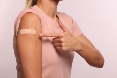 Woman pointing at adhesive bandage on arm after vaccination on light background, closeup