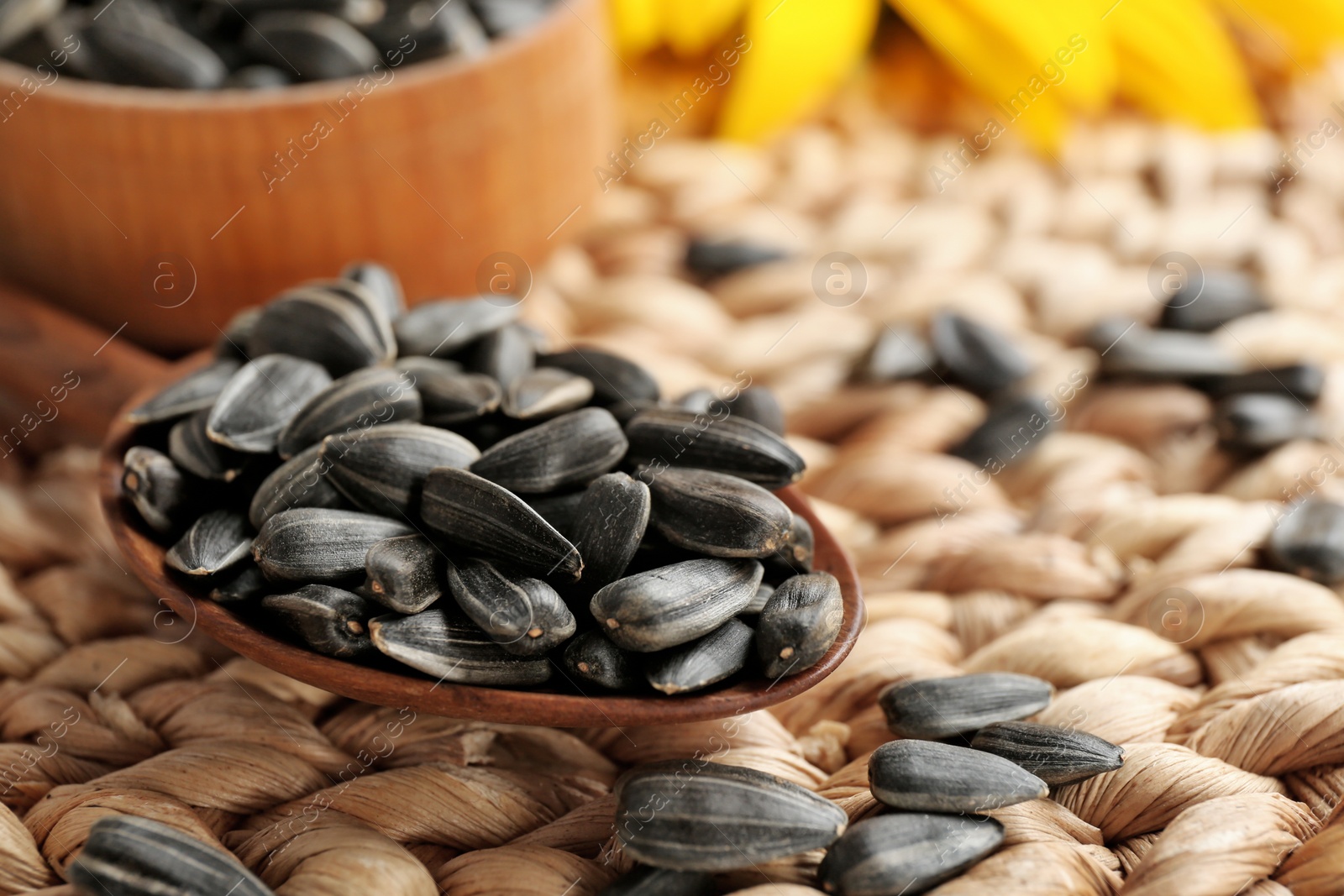 Photo of Spoon with sunflower seeds on wicker mat, closeup