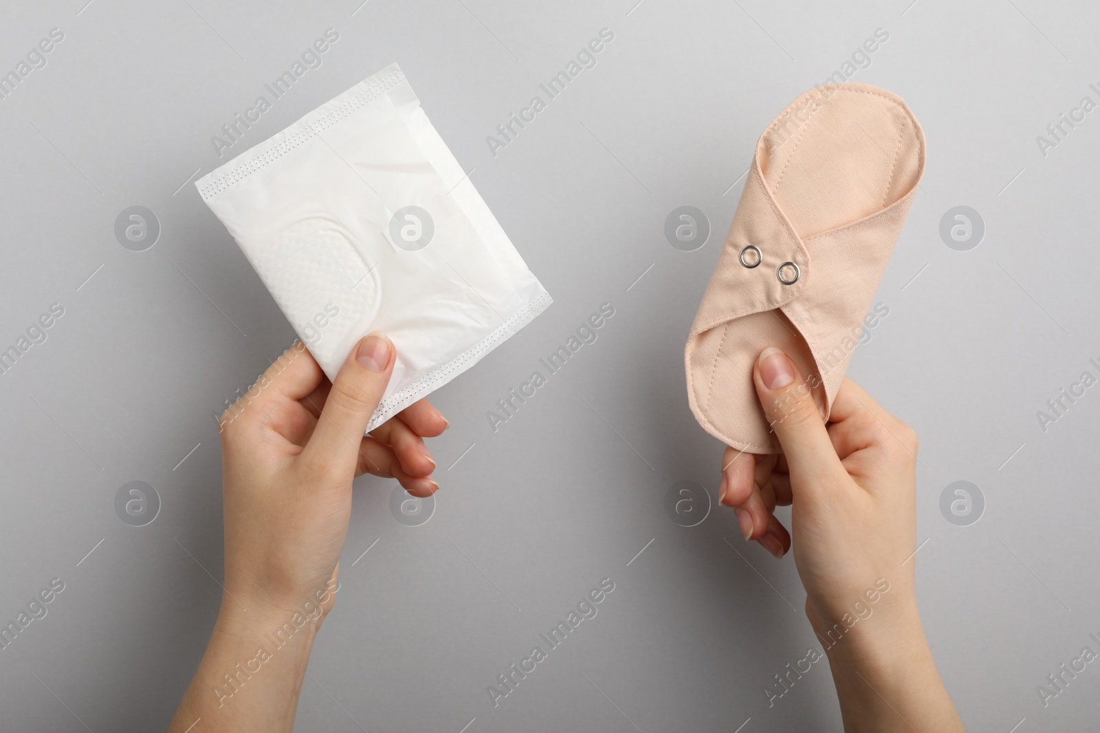 Photo of Woman holding disposable and reusable cloth menstrual pads on grey background, top view