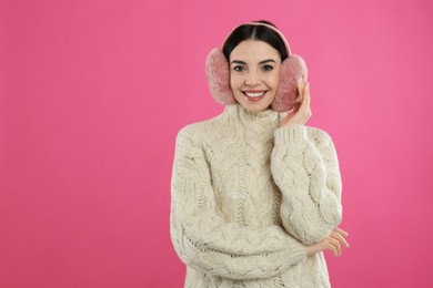 Photo of Beautiful young woman wearing earmuffs on pink background. Space for text