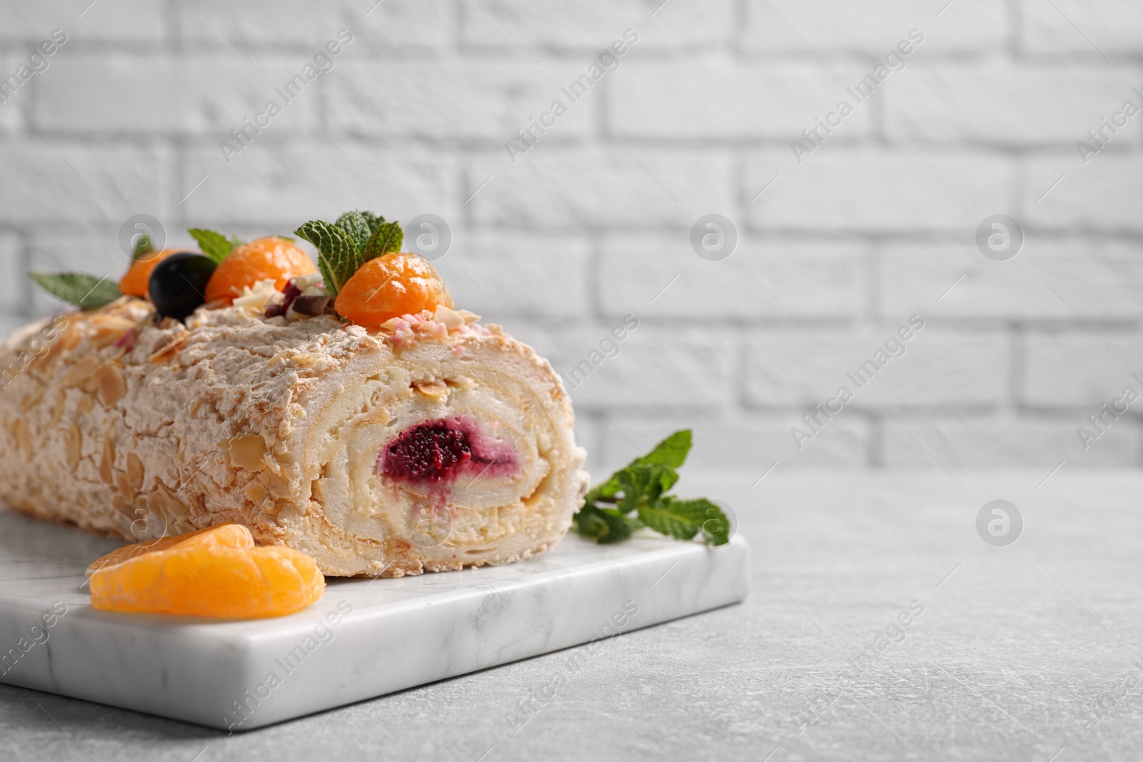 Photo of Tasty meringue roll with jam, tangerine slices and mint leaves on grey table, closeup. Space for text