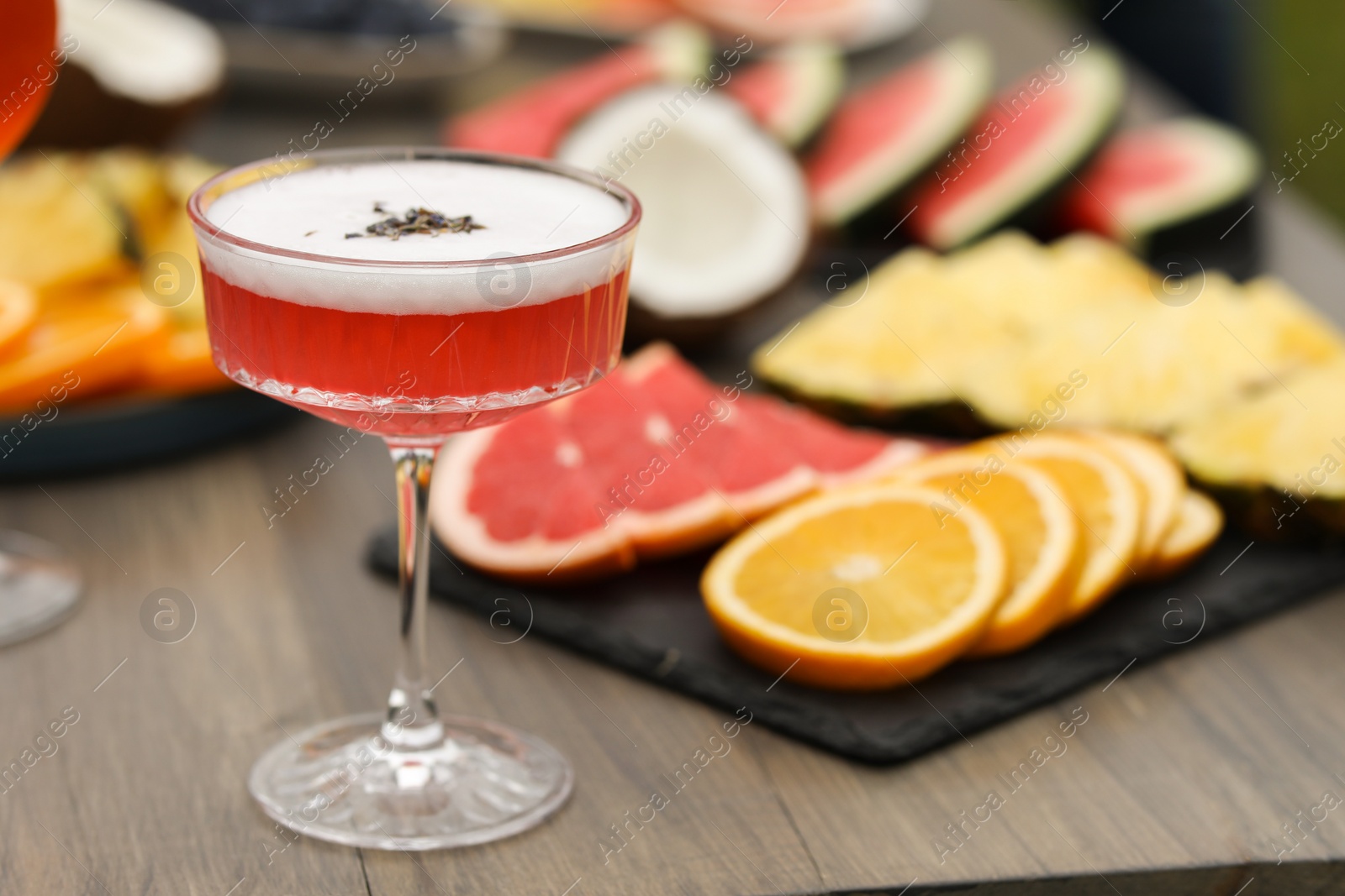 Photo of Glass of cocktail and fruits on wooden table, closeup