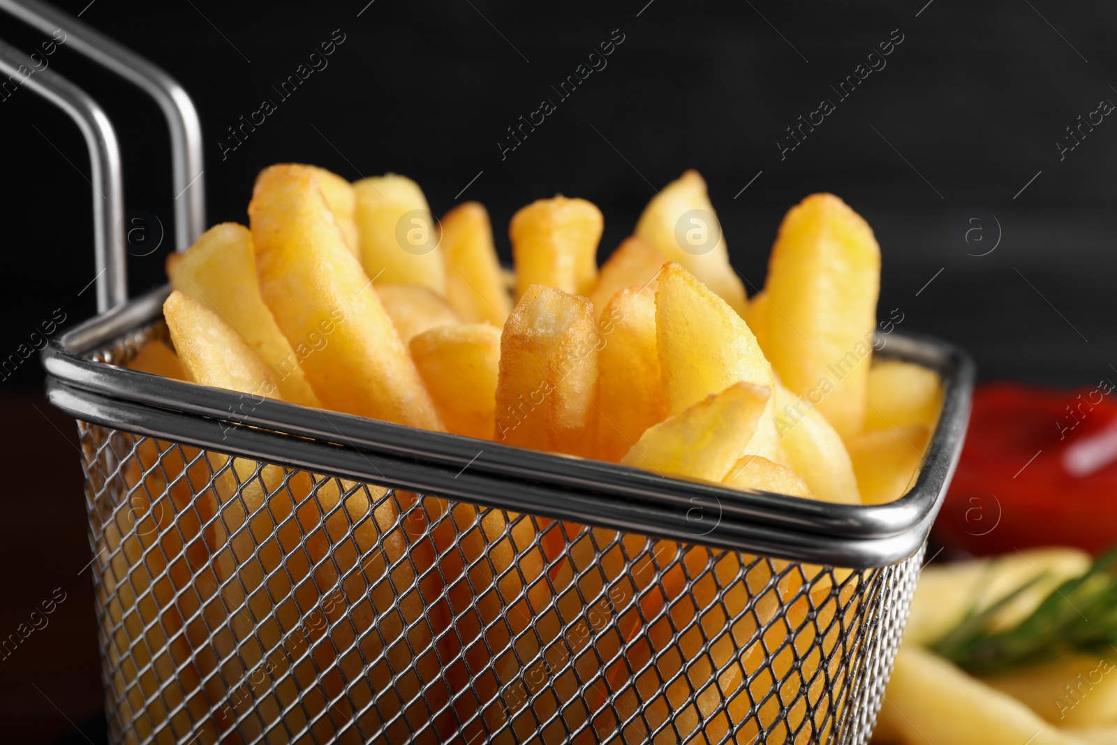 Photo of Frying basket with tasty french fries on blurred background, closeup