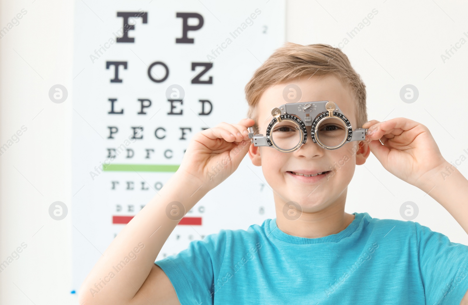 Photo of Little boy with trial frame near eye chart in ophthalmologist office